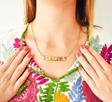 Load image into Gallery viewer, Close-up of a golden artisanal necklace with colorful floral design, worn by a person with a traditional Mexican embroidered blouse in vibrant tones