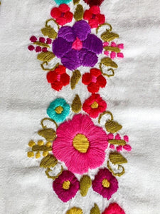 detail of two embroidered pink and purple flowers that decorates a mexican blouse