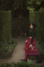 Load image into Gallery viewer, model walking  in a garden wearing a red rebozo as a skirt and a black hat, boots and top