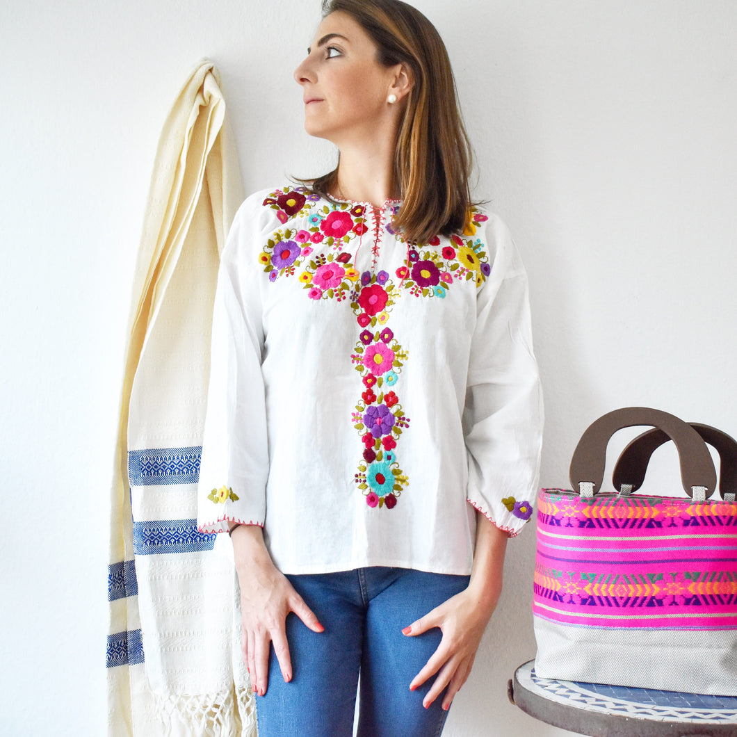 model wearing a white mexican blouse with small and colorful embroidered flowers
